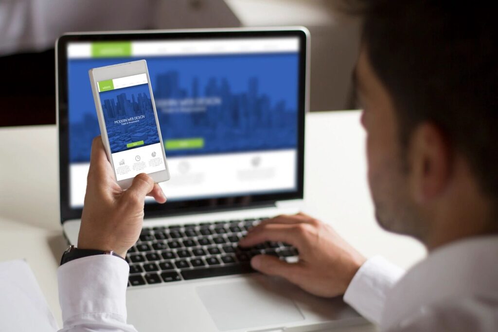 A male looking at a website on a computer and on a cellphone, both websites looks very similar.